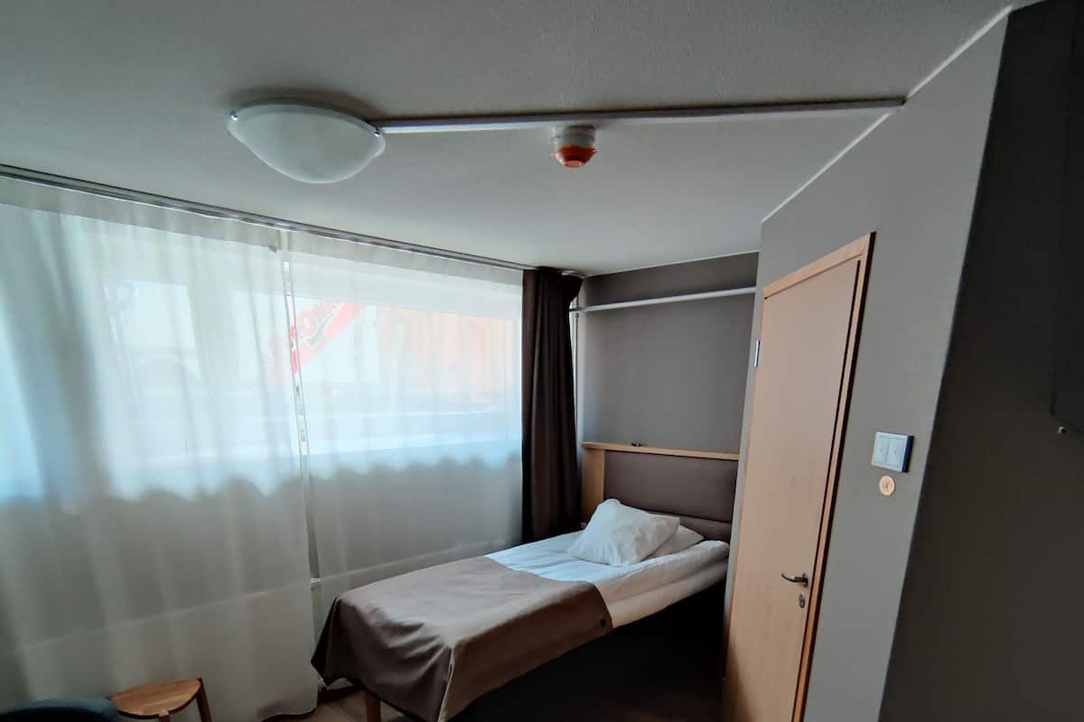 A compact hotel room with a single bed, a small table, a chair, and a sofa.