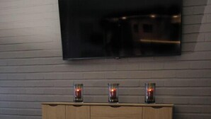 A modern living room with a flat-screen TV mounted on the wall, a wooden cabinet with three candles, and a round coffee table with a remote control. - Hotelli Toivola (Kemi)