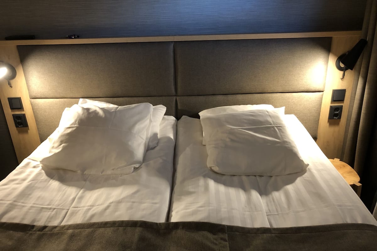 A double bed with white linens and a headboard with integrated lighting.