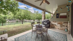 A covered patio with a table and chairs, a ceiling fan, string lights, and a view of a lake and trees. - Rio Refuge Rg 105 2 Bedroom Condo by RedAwning (New Braunfels)