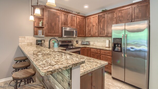 A kitchen with wooden cabinets, a granite countertop, stainless steel appliances, and pendant lighting. - Rio Refuge Rg 105 2 Bedroom Condo by RedAwning (New Braunfels)