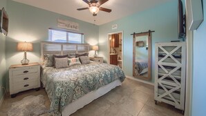 A bedroom with a bed, nightstands, a ceiling fan, a window with blinds, and a mirror. - Rio Refuge Rg 105 2 Bedroom Condo by RedAwning (New Braunfels)
