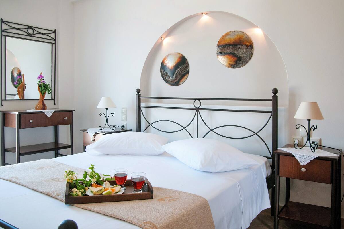 A neatly made bed with white linens, a tray of food and drinks, and two wall art pieces above it.
