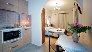 Cucina compatta con forno, zona pranzo con tavolo e sedie, e camera da letto con letto e comodino.