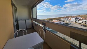 Un balcon avec une table et des chaises, donnant sur une zone côtière avec des bâtiments et une vue sur la mer.
