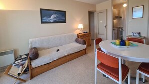 Une pièce confortable avec un canapé, une petite table entourée de chaises, une lampe et un tableau encadré au mur.