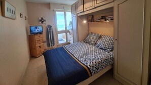 Une chambre avec un lit, une télévision, un étendoir et une armoire.