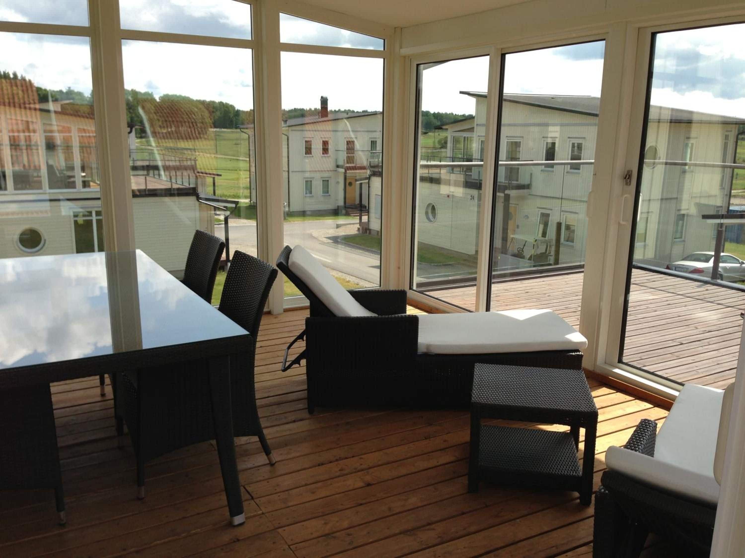 Quarto ensolarado com deck de madeira, uma mesa e cadeiras.