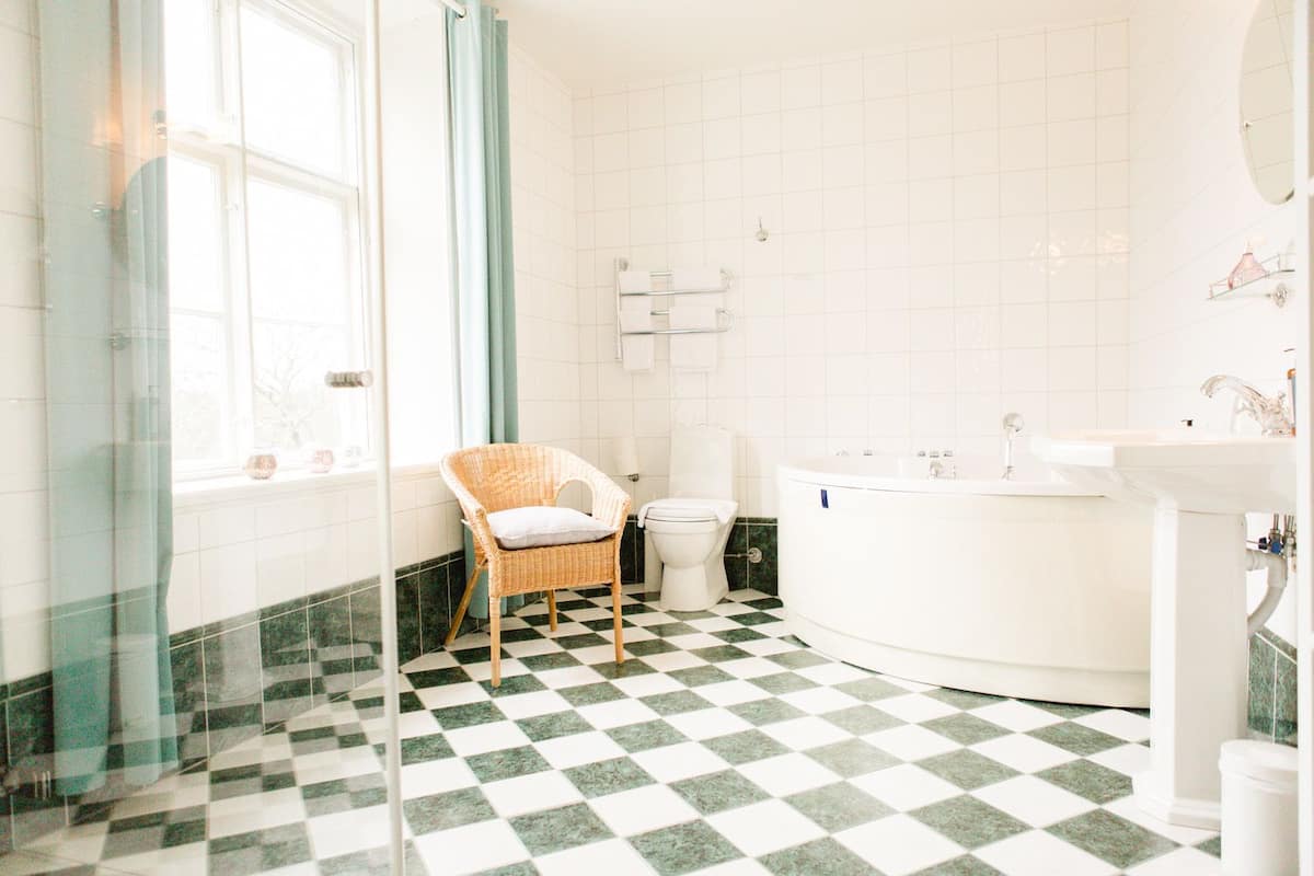 A bathroom with a checkered floor, a wicker chair, a toilet, a bathtub, and a sink.