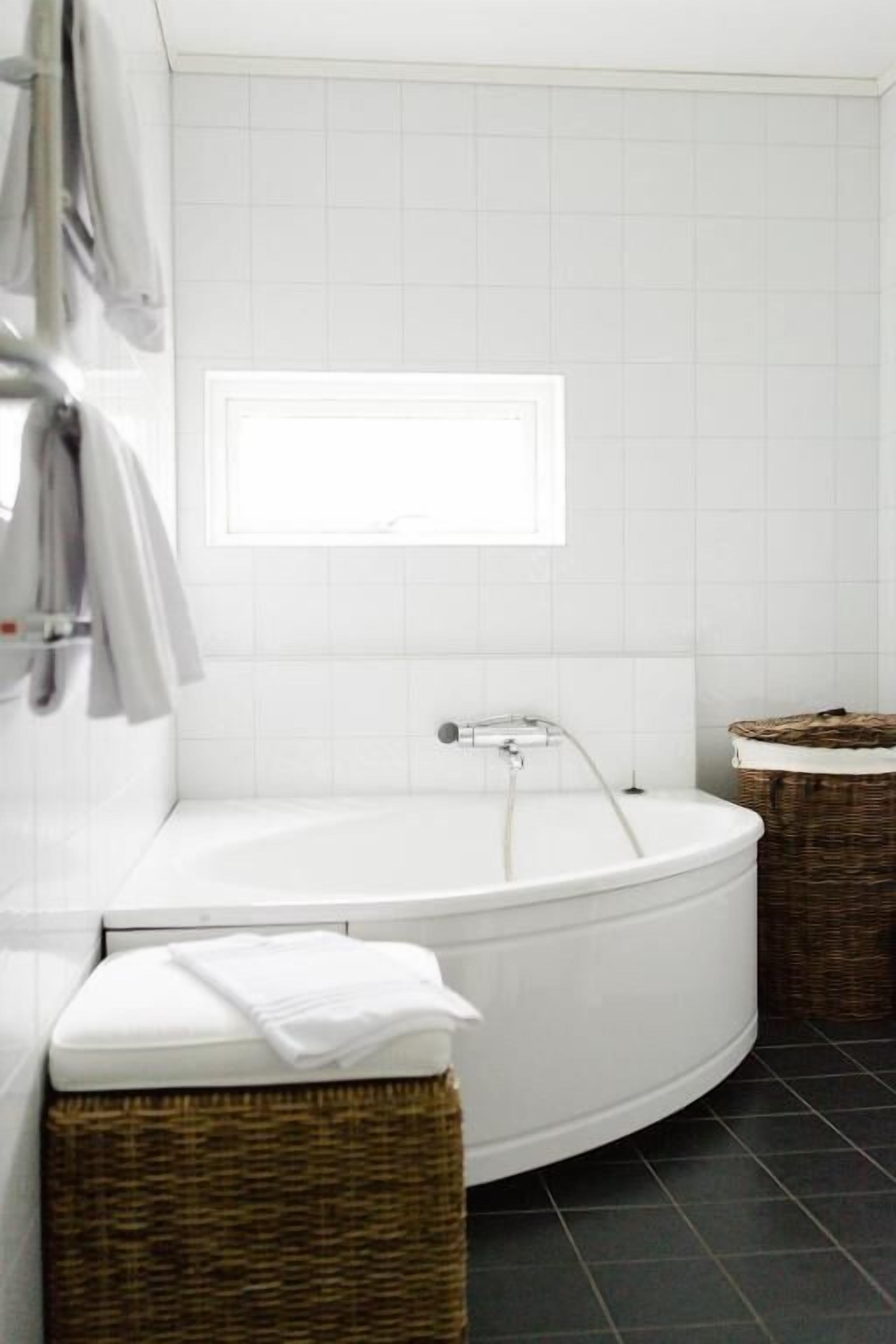 A modern bathroom with a freestanding bathtub, a towel rack, and two wicker baskets.