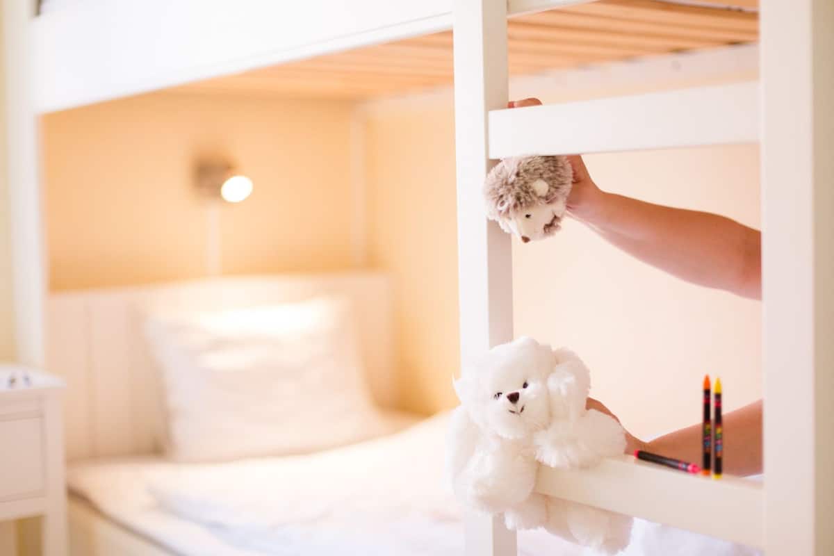 A bunk bed with a white teddy bear on the lower bunk and a stuffed animal on the upper bunk.