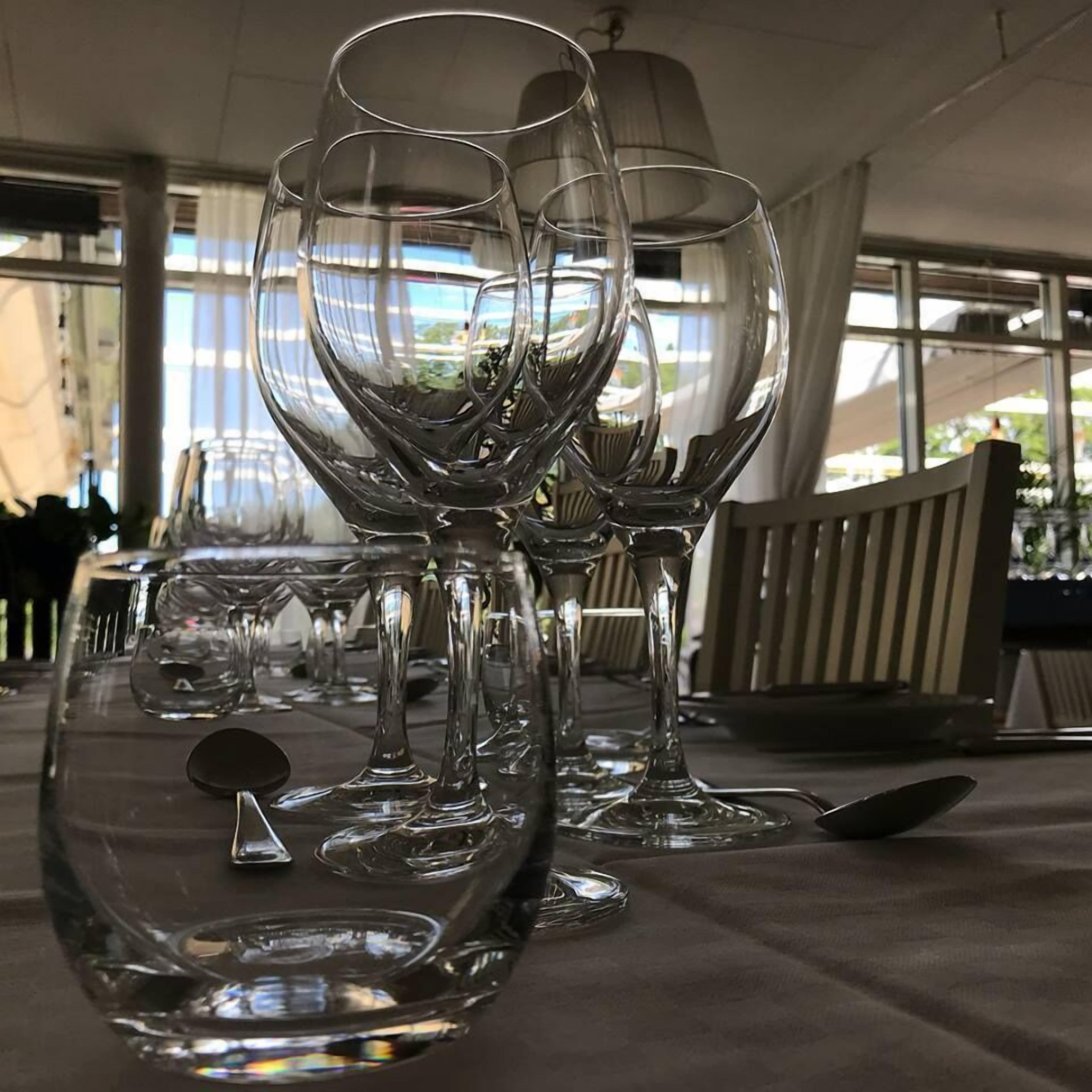 A table with multiple wine glasses and a few spoons, likely in a dining area with large windows and a view outside.