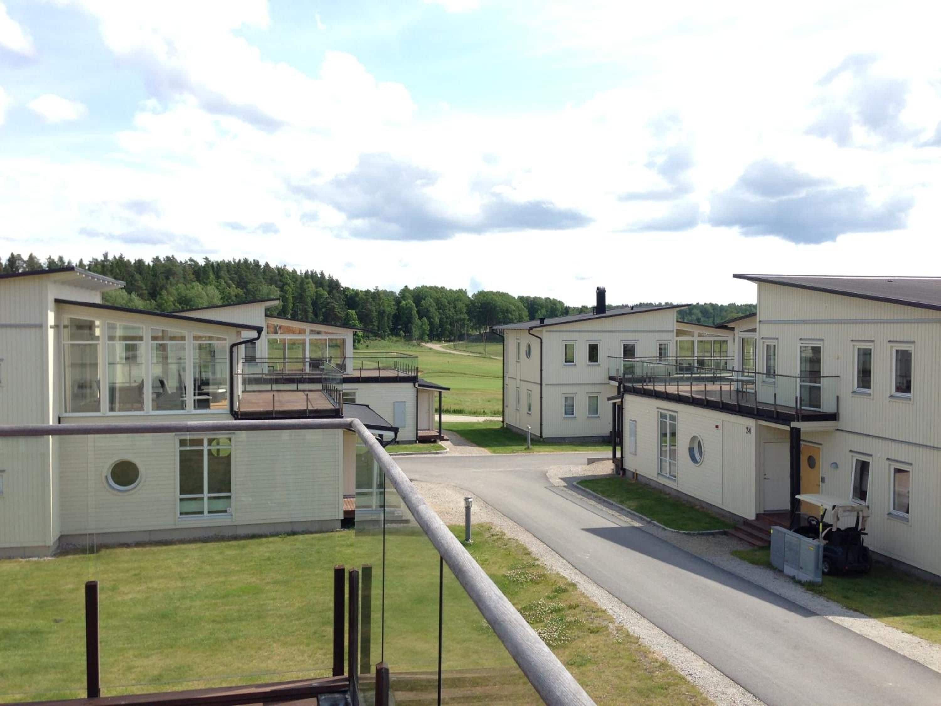 A row of modern, single-story buildings with large windows, a central road, and a grassy area.