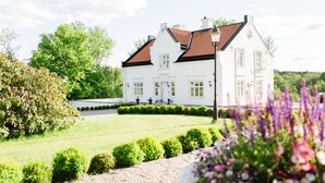 A white building with a red roof, surrounded by well-maintained gardens and trees.