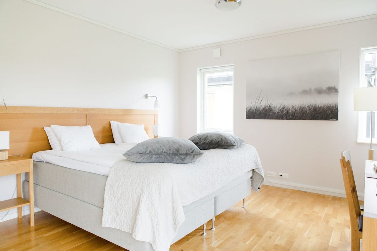 A bedroom with a bed, bedside table, lamp, and a painting on the wall.