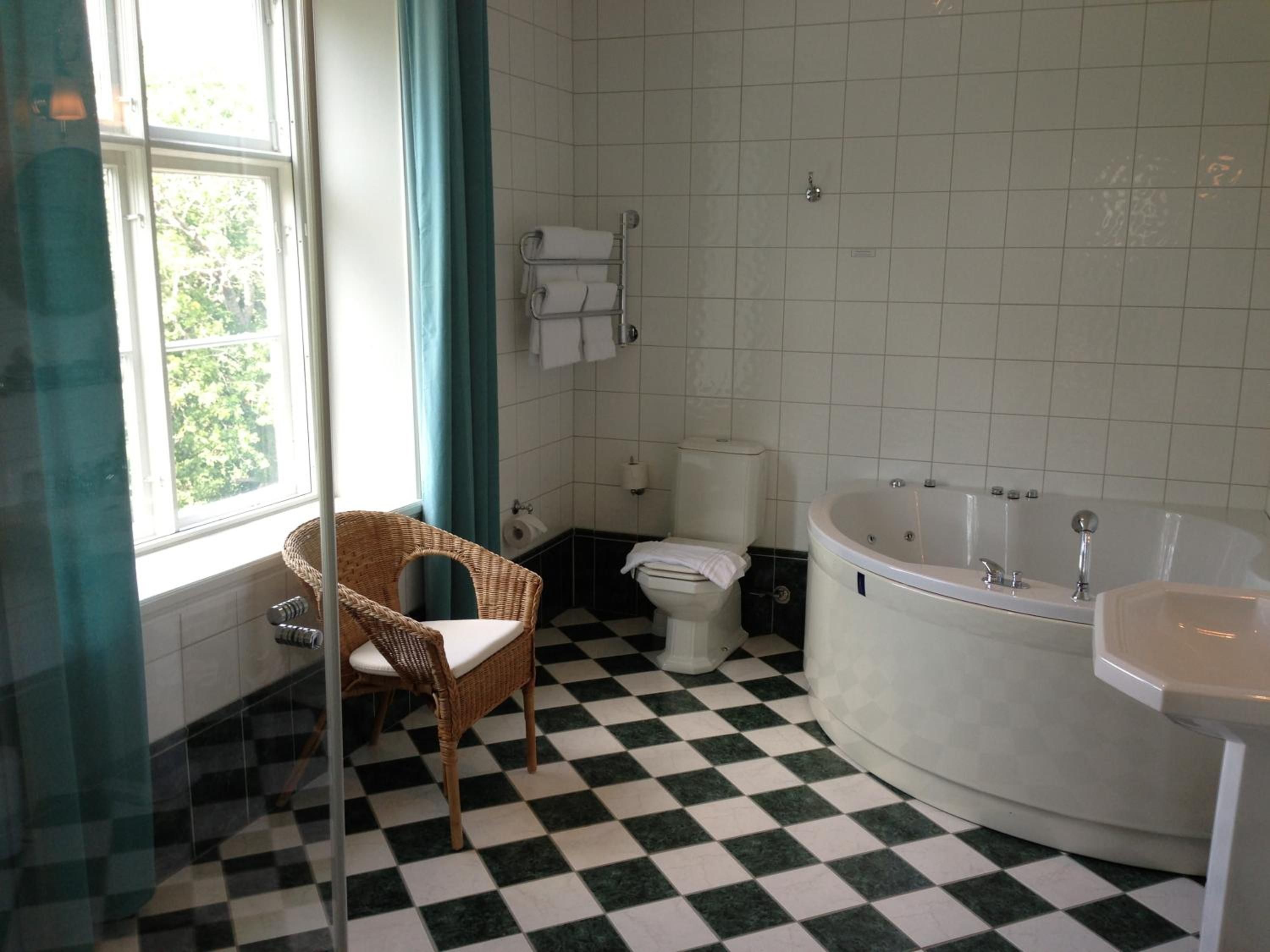 Un baño con piso de tablones, una bañera, un inodoro y una silla de mimbre.