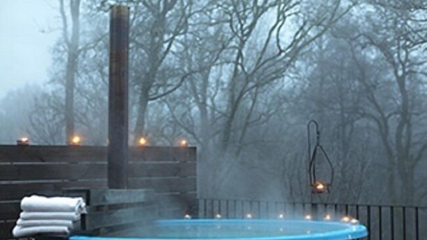A hot tub surrounded by a wooden deck and trees, with a misty background.