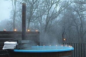 A hot tub surrounded by a wooden deck and trees, with a misty background. - Vidbynäs Gård & Konferens (Nykvarn)