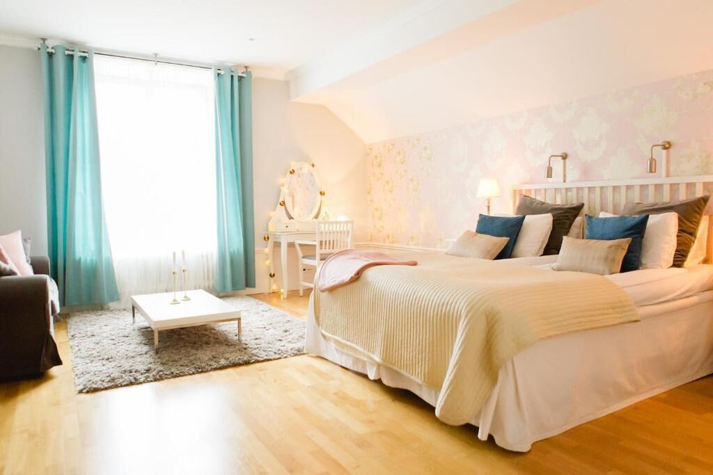 Ein Schlafzimmer mit Bett, Nachttisch, Lampe und einem Fenster mit Vorhängen.