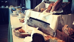A buffet table with various breads, croissants, and a loaf of bread on a wooden board.