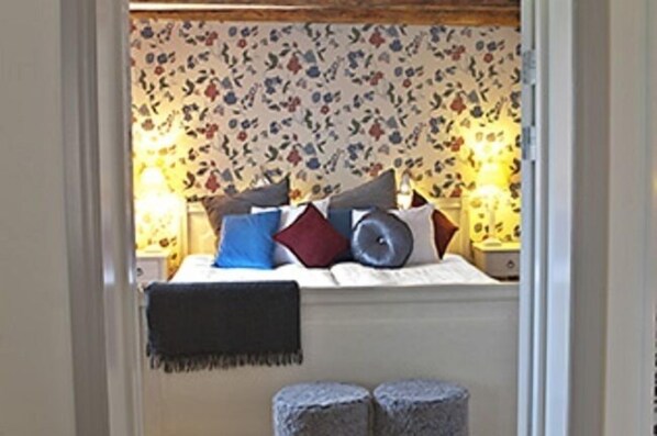 A bedroom with a bed, pillows, a blanket, and a window with floral wallpaper. - Vidbynäs Gård & Konferens (Nykvarn)