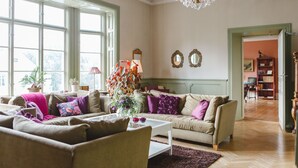 A spacious living room with large windows, a chandelier, and a cozy seating area.
