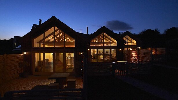 Una casa moderna con amplios ventanales y un interior bien iluminado al anochecer.