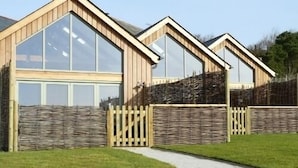 Una hilera de casas modernas con estructura de madera y ventanas amplias, con un camino de grava que conduce a una entrada con portón.