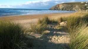 Un paisaje costero con una playa arenosa, dunas cubiertas de hierba y un acantilado con estructuras blancas.