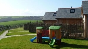 Un parque infantil con toboganes y estructuras para escalar en una zona verde, con vistas a colinas al fondo.