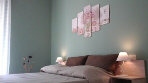 A bedroom with a bed, two bedside tables with lamps, a wall-mounted artwork, and a window with curtains. - Omega House (Guardia Piemontese)
