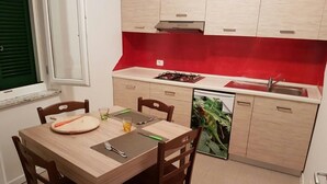 A compact kitchen with a dining table, chairs, a stove, and a dishwasher. - Omega House (Guardia Piemontese)