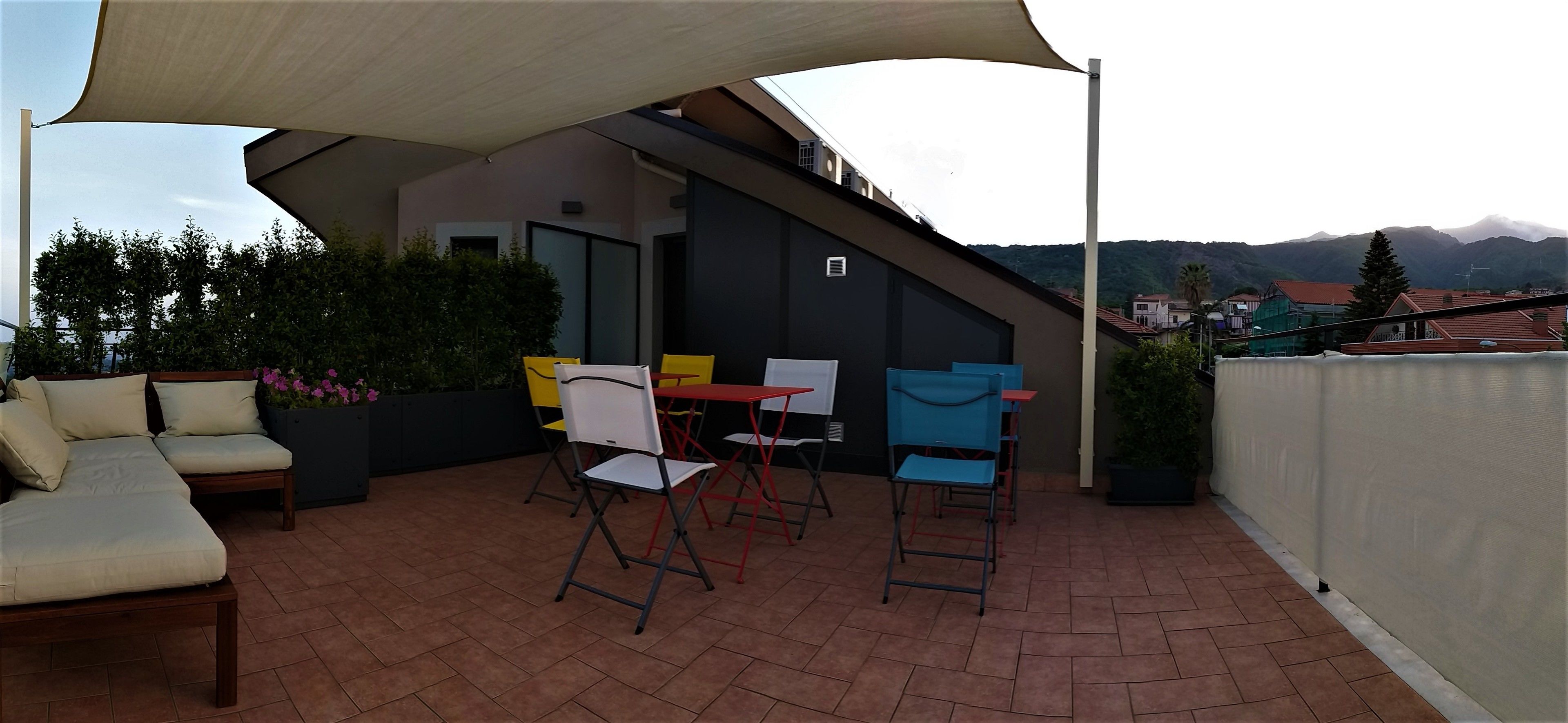 Um terraço ao ar livre com sofá, cadeiras e mesa sob um toldo.