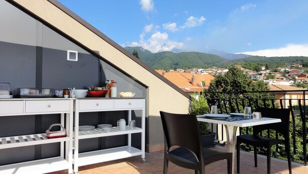 A balcony with a dining setup, including a table, chairs, and a shelf with dishes and condiments. - Etna Sunrise B&B (Zafferana Etnea)