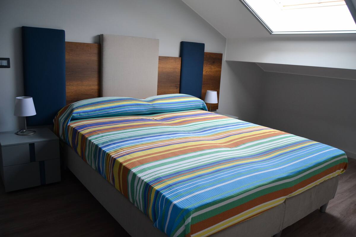 A modern bedroom with a skylight, a striped bedspread, and bedside lamps.