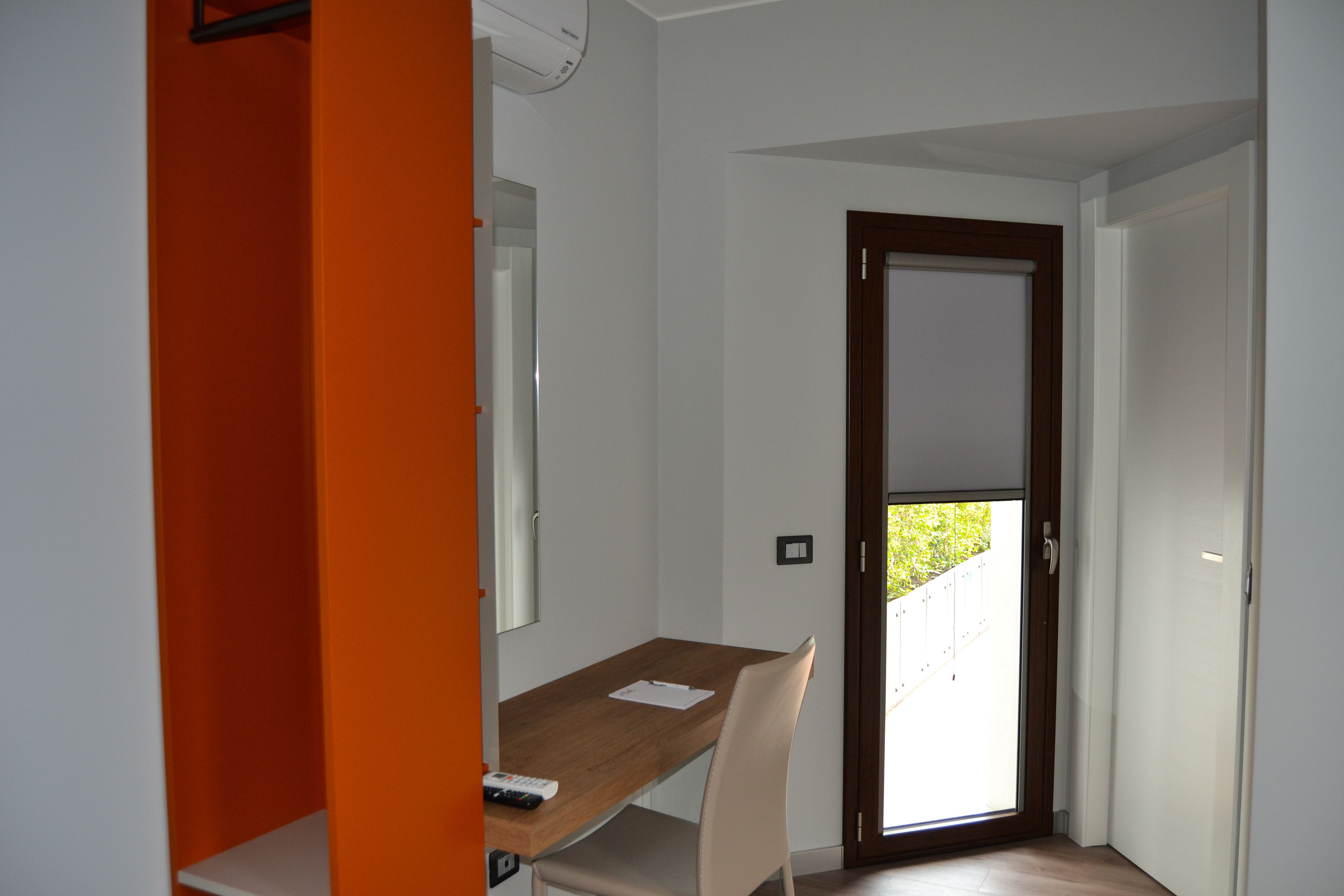 A room with a wooden desk, a chair, a white wall, and a door leading outside.