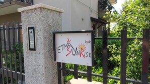 A sign with the text "ETNA SUNRISE" and a sun illustration, mounted on a pillar near a gate. - Etna Sunrise B&B (Zafferana Etnea)