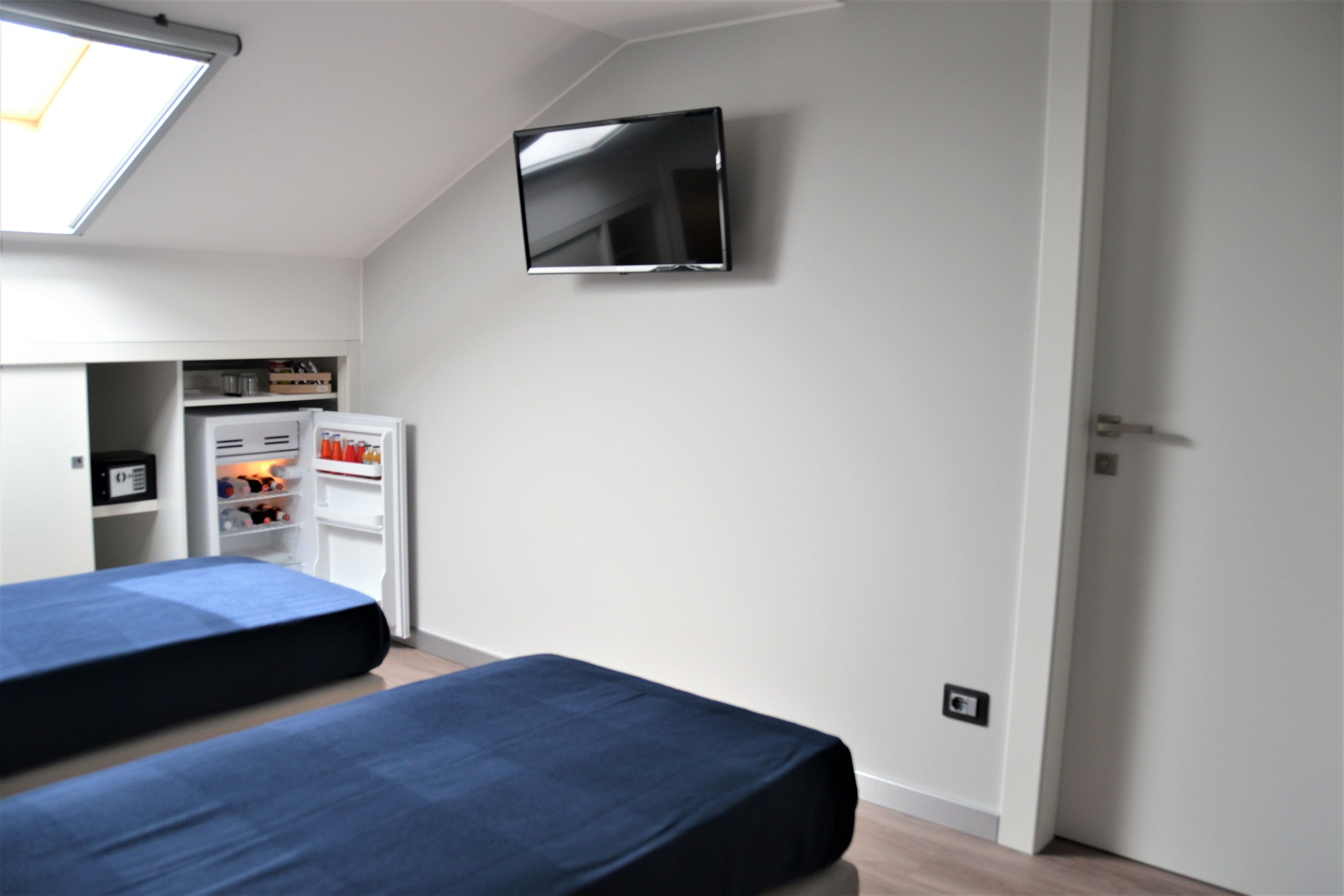 A bedroom with two beds, a TV mounted on the wall, a wardrobe, and a small kitchenette.