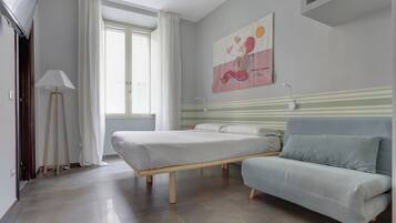 Un dormitorio con cama, sofá, un cuadro en la pared y ventana con cortinas.