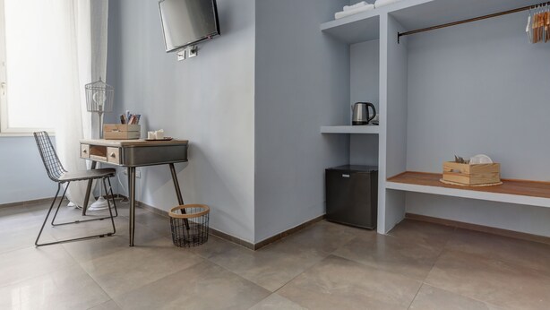 A modern room with a desk, chair, TV, shelves, and a small refrigerator. - Appartamento Capo D'Africa 30 (Rome)