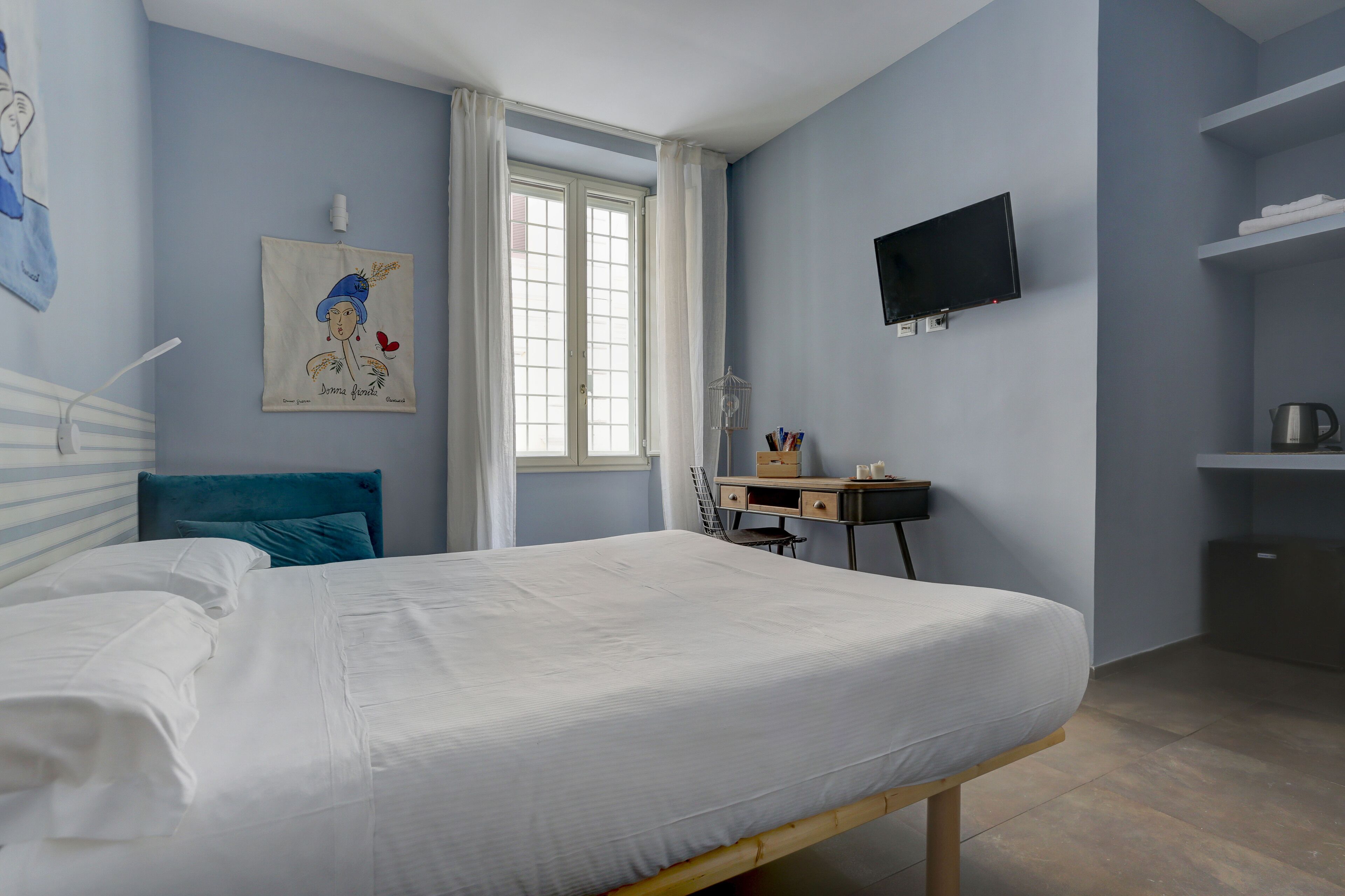 A bedroom with a bed, a desk, a chair, a TV, and a window.