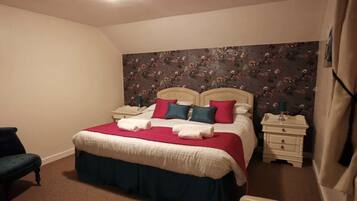 Un dormitorio con una cama, dos mesitas de noche, una silla y un papel tapiz con motivos florales.