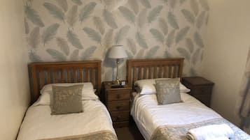 A room with two single beds, each with a wooden headboard, a nightstand, a lamp, and a patterned pillow.