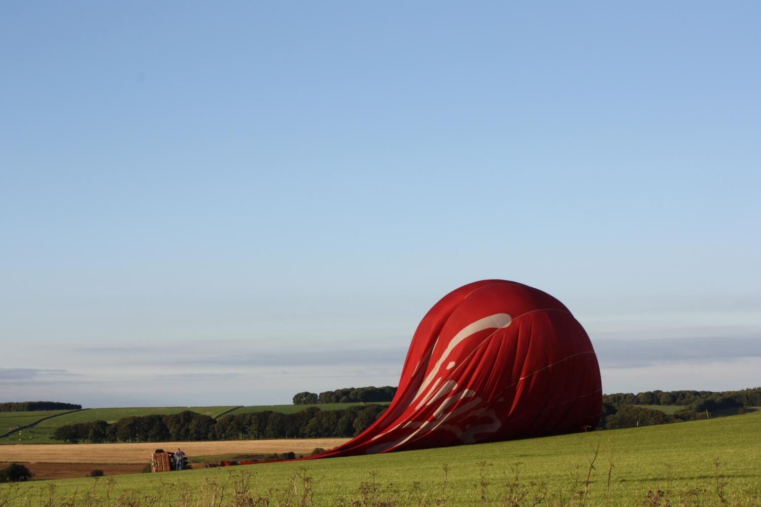 A red hot air balloon in a field with a clear sky.