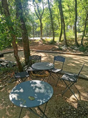 Een terras met een ronde tafel en stoelen, omringd door bomen.