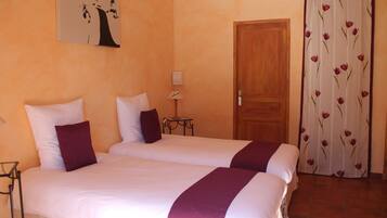 A hotel room with two beds, a wooden door, a small table with a lamp, and a floral curtain.
