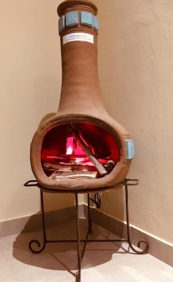 A traditional clay stove with a metal stand, a visible fire inside, and a label on the front. - C9 at Diani Beachalets (Diani Beach)