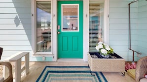 A teal door with a number 201, a small porch area with wicker furniture, and a woven planter with flowers. - Close to Beach, Pet Friendly and Shared Pool (Port Aransas)