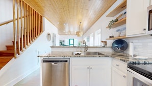 A modern kitchen with white cabinets, a stainless steel dishwasher, and a wooden staircase. - Close to Beach, Pet Friendly and Shared Pool (Port Aransas)