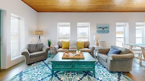 A cozy living room with a wooden ceiling, two sofas with yellow cushions, a coffee table, and a patterned rug. - Close to Beach, Pet Friendly and Shared Pool (Port Aransas)